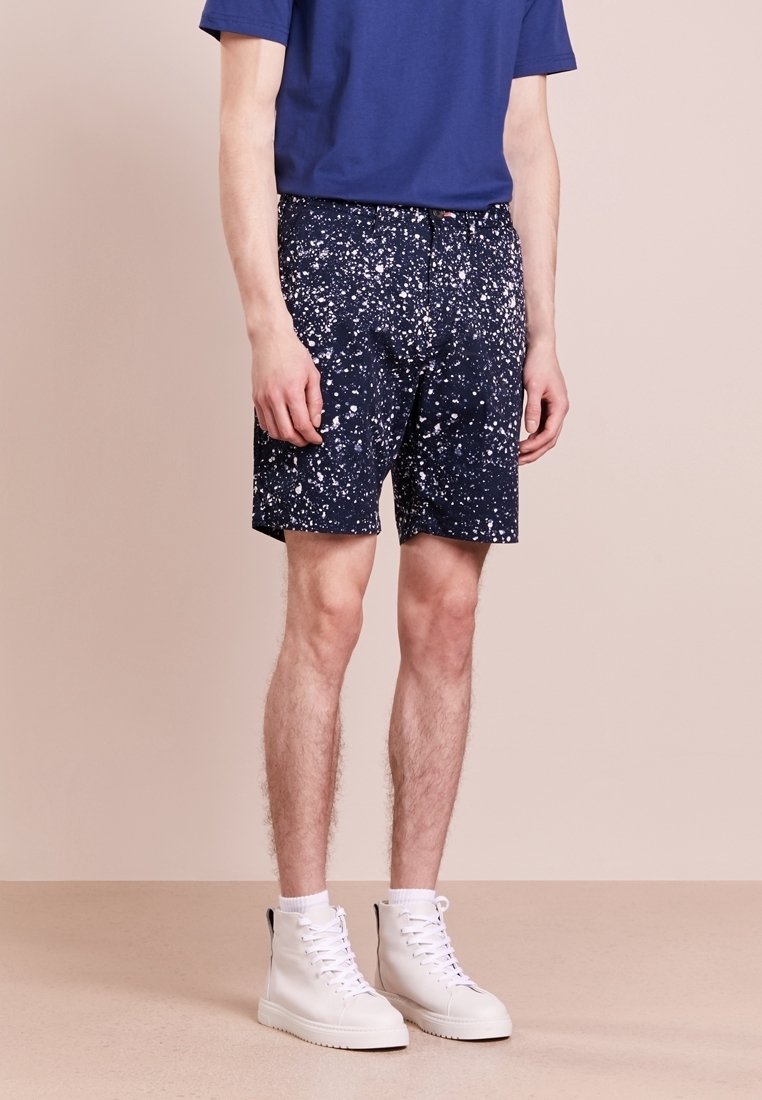 Granatowe szorty z białym wzorem plam, wykonane z lekkiego materiału. Połączone z niebieską koszulą z krótkim rękawem i białymi trampkami za kostkę.