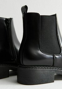 Botas Chelsea negras de piel lisa, con paneles laterales elásticos y una suela texturizada. Presentan una cremallera lateral y un tacón plano y robusto.