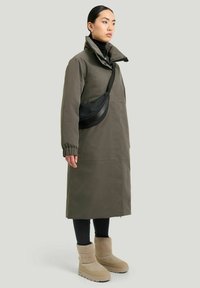Olivenfarvet vandtæt jakke med høj krave, sort crossbody taske, sorte leggings og beige ankelstøvler med plateau-sål.