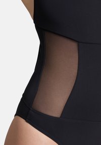 Maillot de bain noir avec un haut en tissu solide et des panneaux latéraux en mesh transparent, mettant en valeur une silhouette élégante et une texture lisse.