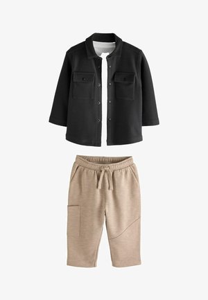 Fekete gombos dzseki két mellzsebbel, bézs jogger nadrággal párosítva, rugalmas derékrésszel és oldalzsebbel.