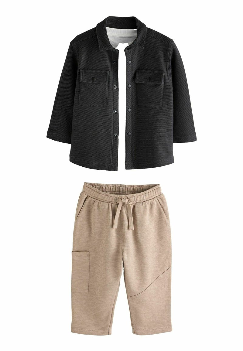 Schwarze Knopfleistenjacke mit zwei Brusttaschen, kombiniert mit beigen Jogginghosen mit elastischem Bund und Seitentasche.