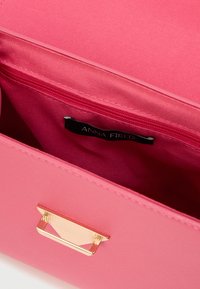 Sac à main synthétique rose avec une texture lisse, une quincaillerie dorée à l'avant et une poche intérieure étiquetée. La doublure intérieure correspond à la couleur extérieure.