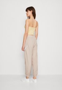 Hellgelbes ärmelloses Oberteil, kombiniert mit beigen, elastischen Hosen mit Seitentaschen, Bündchen und weißen Sneakers. Minimalistisches Design.