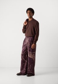 Camisa marrón de mangas largas combinada con pantalones de pierna ancha morados que presentan un patrón temático de mapas con acentos en beige claro, de textura suave.