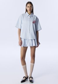 Blue and white striped short-sleeve shirt with a red embroidered initial, paired with a matching pleated skirt and knee-high beige socks.