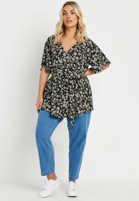 Top avvolgente nero a fiori con maniche corte e vita con laccio, abbinato a jeans in denim blu e sneaker bianche. Presenta motivi di margherite.