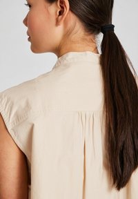 Beige, ärmlös blus med krage, med en detalj av bakre plisséer. Slätt bomullstyg med en avslappnad passform.