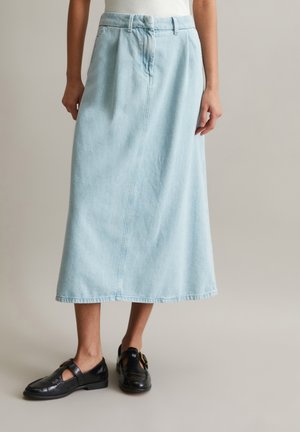 Jasnoniebieska dżinsowa spódnica midi o prostym kroju, z szlufkami na pasek, plisami z przodu i czystym dołem. Noszona z czarnymi skórzanymi butami.