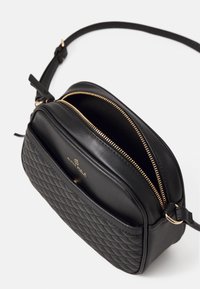 Borsa a tracolla nera trapuntata con zip dorata e tracolla regolabile, dotata di una piccola tasca frontale con chiusura a battente.