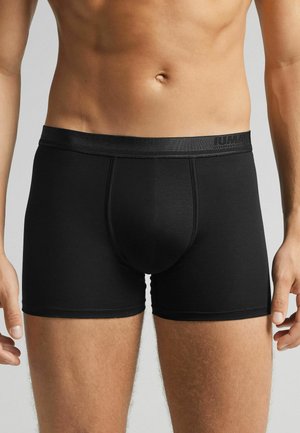 Schwarze Boxershorts aus dehnbarem Material mit glatter Oberfläche, ausgestattet mit einem elastischen Bund mit Branding und einem enganliegenden Design.