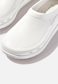 Witte instapklompen met een gladde, matte afwerking, textuuraccenten aan de zijkant en een ademend bovenwerk voor ventilatie. Lichtgewicht rubberen zool.