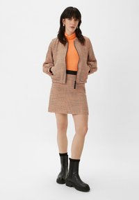 Houndstooth bomberjack in oranje en zwart, gecombineerd met een aansluitende oranje coltrui en bijpassende rok, aangevuld met zwarte enkellaarsjes.
