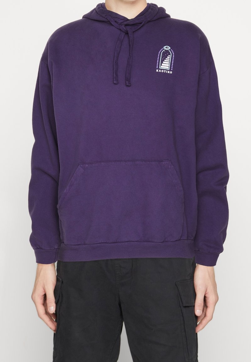 Lila bomullshuvtröja med en framficka, dragband kapuschong och en grafisk logotyp på bröstet. Har ribbade muddar och nederkant.