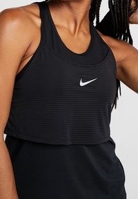 Sort atletisk crop top med ribbet tekstur, der har en rund halsudskæring og et lille hvidt Nike-logo foran.