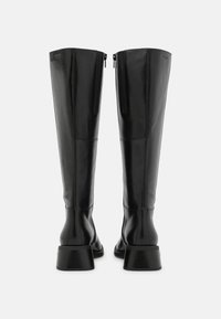 Botas de cuero negro hasta la rodilla con una textura suave, cierre de cremallera en la parte posterior y un tacón grueso. Diseño minimalista, sin patrones visibles.