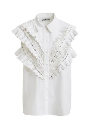 Camicia bianca senza maniche con bottoni, colletto appuntito, volant sovrapposti e bordo in pizzo che forma una V sul davanti.