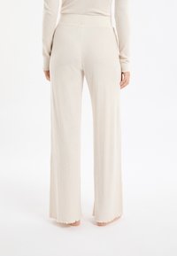 Beżowe szerokie spodnie palazzo z prążkowanego dzianiny, z szerokimi nogawkami, elastycznym pasem i odcięciem w kształcie falbanki. Miękka tekstura i luźny krój.