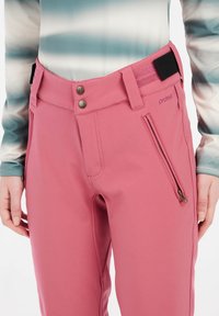 Roze softshellbroek met hoge taille, twee voorzakken en metalen knopen, inclusief een ritszak aan de zijkant en een merklabel.