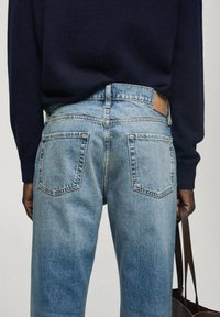 Jeans de mezclilla azul claro con corte recto, que cuentan con dos bolsillos traseros y una etiqueta de cuero en la cinturilla. Llevados con un suéter oscuro.