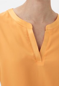 Kortærmet bluse i lyseorange, med V-hals og kontrasterende satinbånd samt en glat, let tekstur.