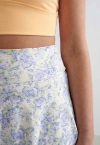 Blumiger Rock mit einem hellen Pastellfarbschema, der Lavendel- und grüne Rosen auf einem cremigen Hintergrund zeigt, mit einem breiten, glatten Taillenbund.