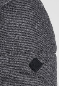 Gorro de punto gris con un patrón texturizado. Presenta un parche de logo en forma de diamante negro con el texto "Pier One". Tela suave y elástica.