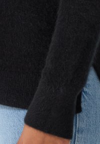 Svart stickad tröja med en mjuk, luddig textur på Ärmen. Manschetten är något åtsittande, kombinerad med ljusblå denim.