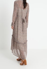 Robe longue et légère à fleurs dans des tons doux de marron et de crème, avec des manches longues, un ourlet à volants et un détail de taille à nouer.