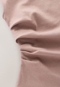 Tissu en coton doux rose clair, drapé et rassemblé, montrant une texture lisse et une légère élasticité, avec des plis subtils et une forme décontractée.