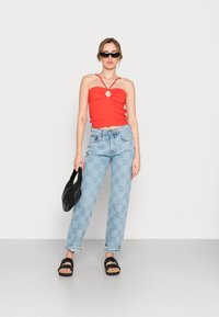 Top cropped vermelho com nervuras e detalhe em forma de olho-chave, jeans xadrez azul claro, sandálias pretas e uma mala preta texturizada.
