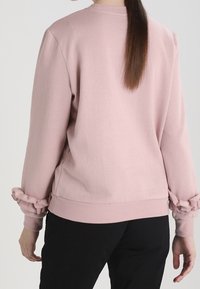 Sudadera rosa de tejido suave, con cuello redondo y acentos fruncidos en las mangas, de corte relajado y con cintura elástica.