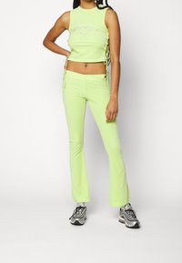 Neongrön crop top med sidoknytningar och dekorationer; utsvängda neongröna byxor med dragsko. Bärs med grå och svarta sneakers.