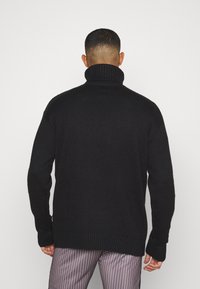 Schwarzer Strickpullover mit hohem, geripptem Rollkragen. Weit geschnitten mit gerippten Bündchen, die einen strukturierten Stoff präsentieren.