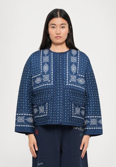 Veste matelassée bleu marine avec des motifs brodés blancs, dotée de deux poches avant et d'un col rond. Tissu texturé avec un design de coutures.