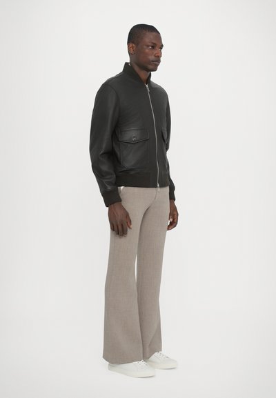 Chaqueta bomber de cuero negro con dos bolsillos frontales, puños acanalados y un cuello alto. Combinada con pantalones acampanados beige y zapatillas blancas.