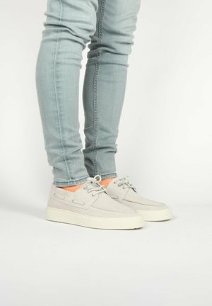 Gray suede sneakers with a low profile, round toe, and white rubber sole. Features laces and side detailing. Worn with light blue skinny jeans.