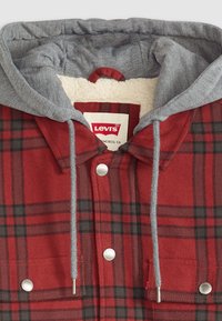 Red and black plaid flannel shirt with a gray hoodie, featuring a soft lining, silver snap buttons, and dual chest pockets.