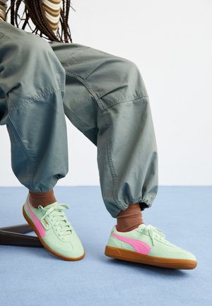 Light green sneakers with pink accents and a brown rubber sole, featuring textured material and a rounded, casual design.