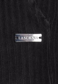 Black ribbed fabric with a shiny silver rectangular tag displaying "LASCANA." Textured surface with vertical lines.