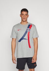 Siva pamučna majica s izraženim plavim i crvenim potezima četkice, s logom Pariza na lijevoj strani prsnog koša i Nike logom na ramenu.