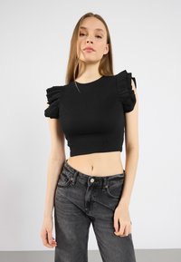 Černý žebrovaný crop top s volánkovými rukávy, spárovaný s tmavě šedými džíny s vysokým pasem. Hladká textura a přiléhavý střih.