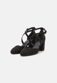 Chaussures à talons hauts pour femmes en daim noir, bouts pointus, avec brides croisées à la cheville et boucles sur fond blanc uni.