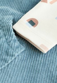 Light blue ribbed fabric with a soft texture, layered with a cream-colored sleeve featuring abstract pastel shapes and neat stitching.