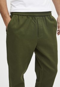 Olivengrønne sweatpants med elastisk talje, sidelommer og blødt, tekstureret stof. Casual design velegnet til afslappet brug.