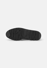 Semelle de chaussure noire avec un motif de bande de roulement texturé et le nom de la marque "Tamaris" embossé au centre, taille 37 indiquée près du logo.