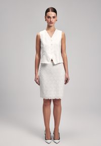 Witte tekstuurlussenloze blazer met knopen en een bijpassende knielange rok met gegolfde zoom en bloemmotieven. Hakken maken de look compleet.