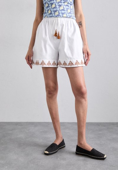 White elastic waistband shorts with intricate brown embroidery at the hem; accompanied by black espadrilles with a textured finish.