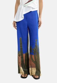 Niebieskie lniane spodnie z nadrukiem krajobrazu kaktusów w zielonym i brązowym kolorze na dolnej krawędzi; szerokie nogawki w gładkiej teksturze.