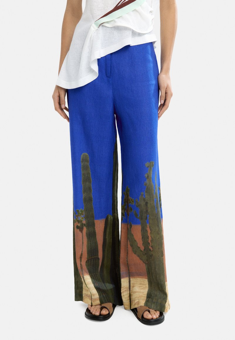Niebieskie lniane spodnie z nadrukiem krajobrazu kaktusów w zielonym i brązowym kolorze na dolnej krawędzi; szerokie nogawki w gładkiej teksturze.